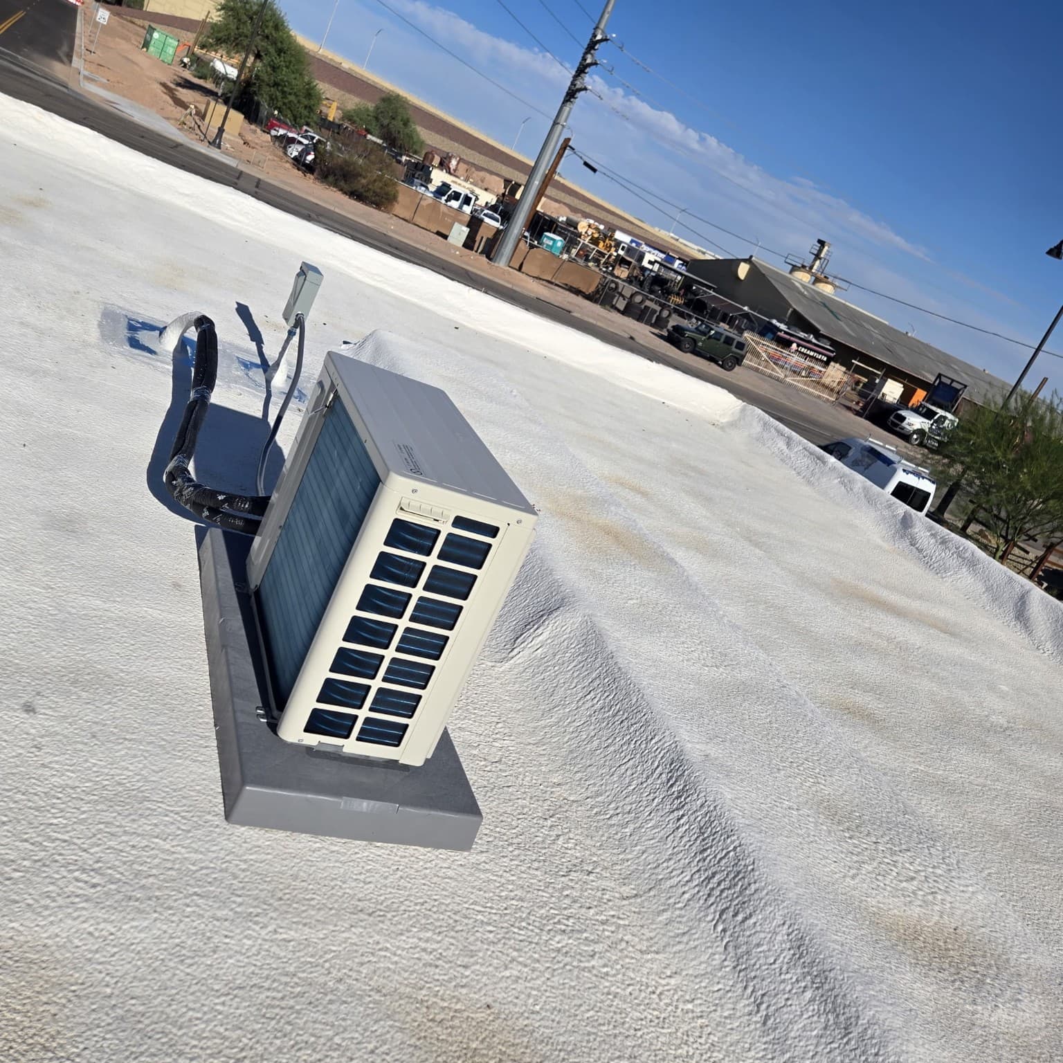 White air conditioning unit mounted on a textured white roof overlooking a commercial industrial area.