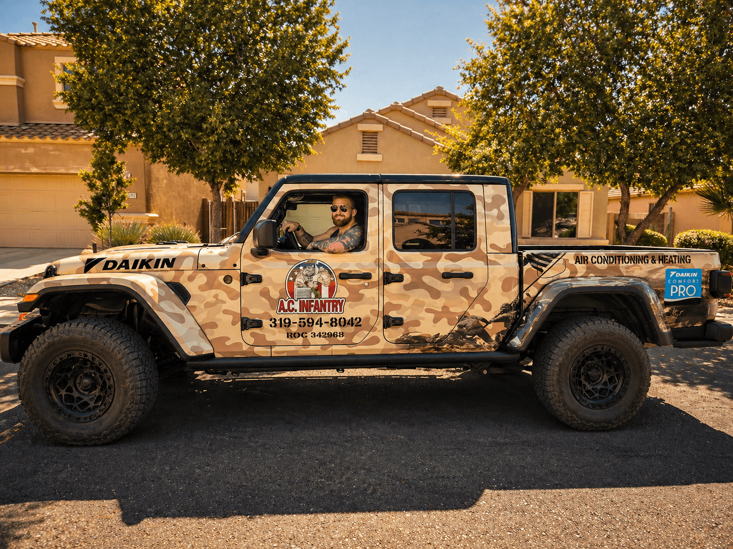 Man driving a desert camouflage Jeep Gladiator with A.C. Infantry branding on a suburban street.