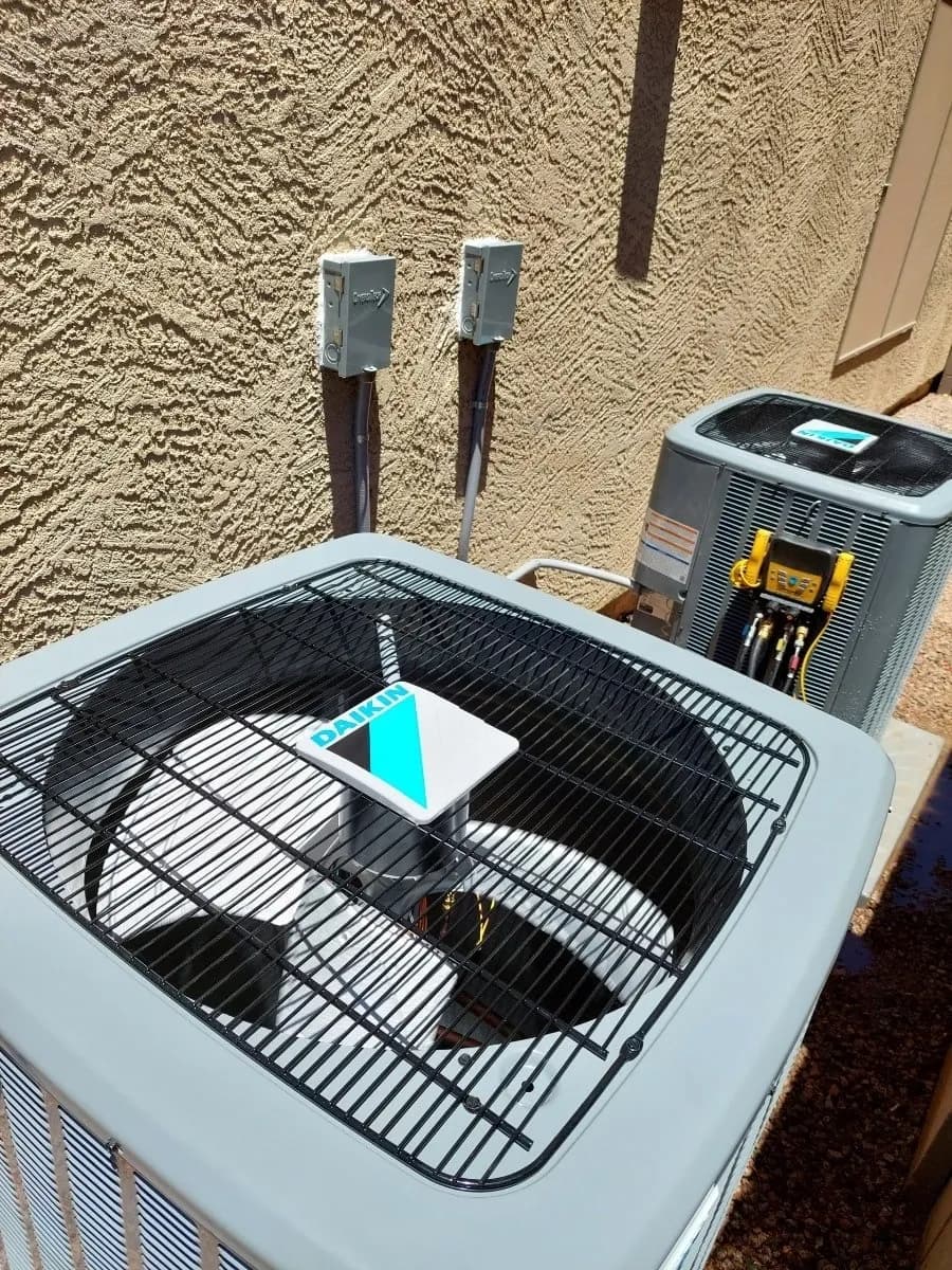 Two Daikin air conditioning units installed outdoors against a tan stucco wall with electrical boxes.